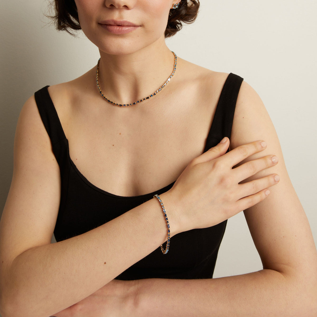 Model. Woman wearing a black top and blue tennis necklace and bracelet against a neutral background.
