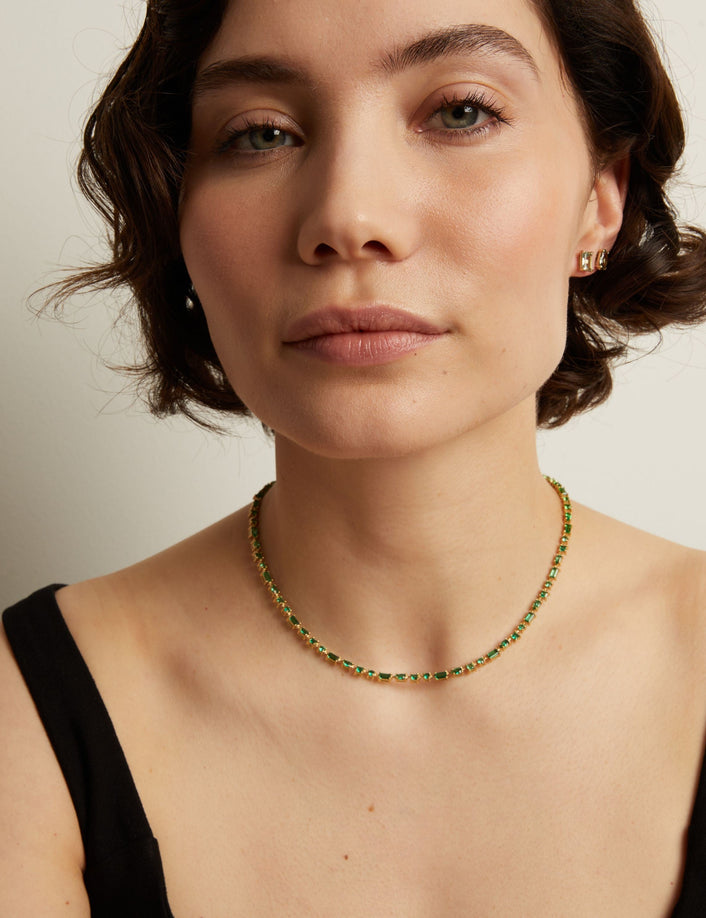 Woman wearing a green tennis necklace against a neutral background. Model