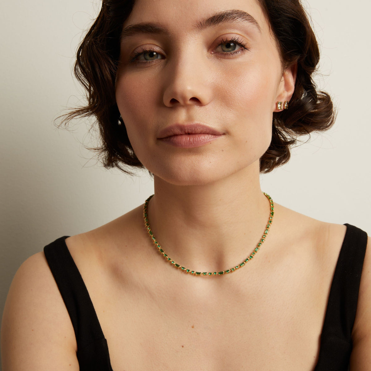 Woman wearing a green tennis necklace against a neutral background. Model