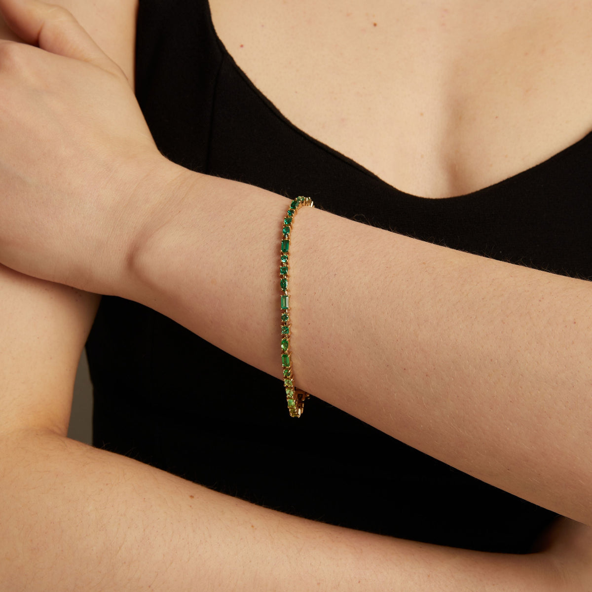 Model. Green tennis bracelet on a person's wrist against a black background.