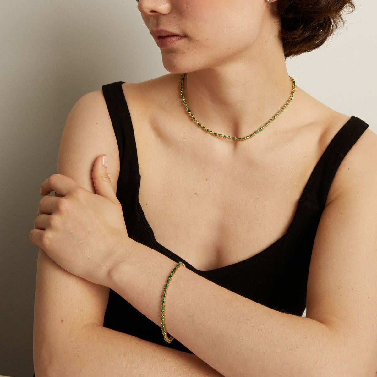 Model. Person wearing a green tennis necklace and bracelet against a neutral background.
