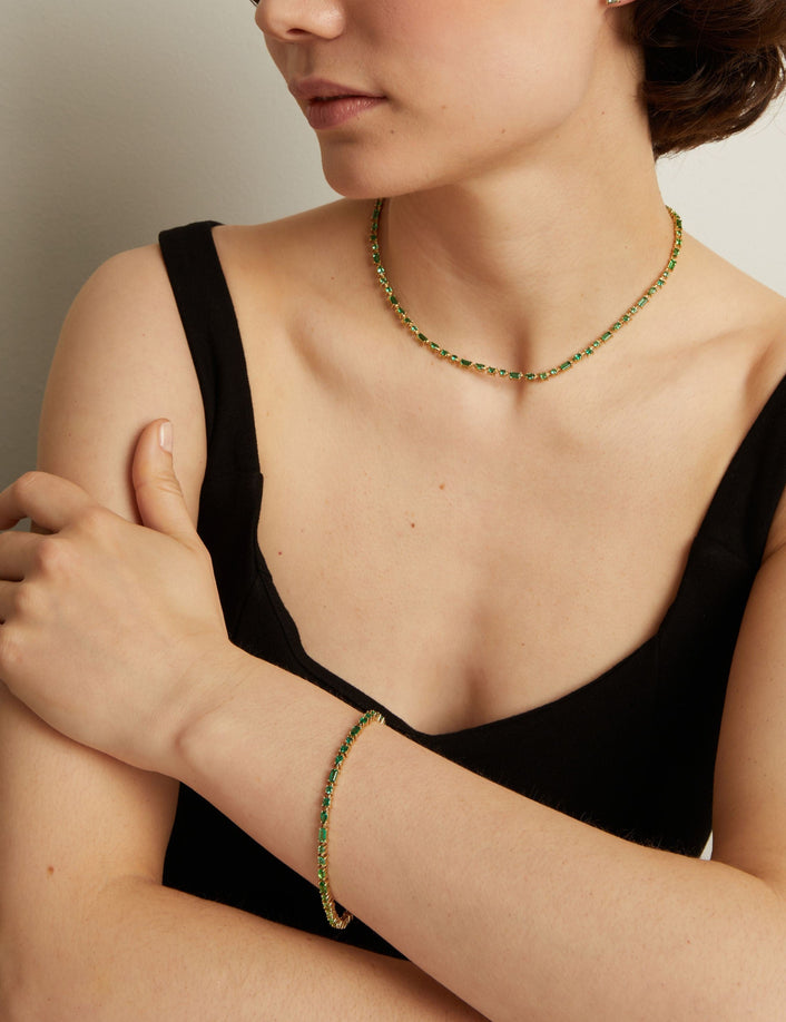 Person wearing a green tennis necklace and bracelet against a neutral background. 