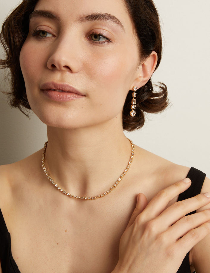 Model. Woman wearing a tennis necklace and earrings against a neutral background
