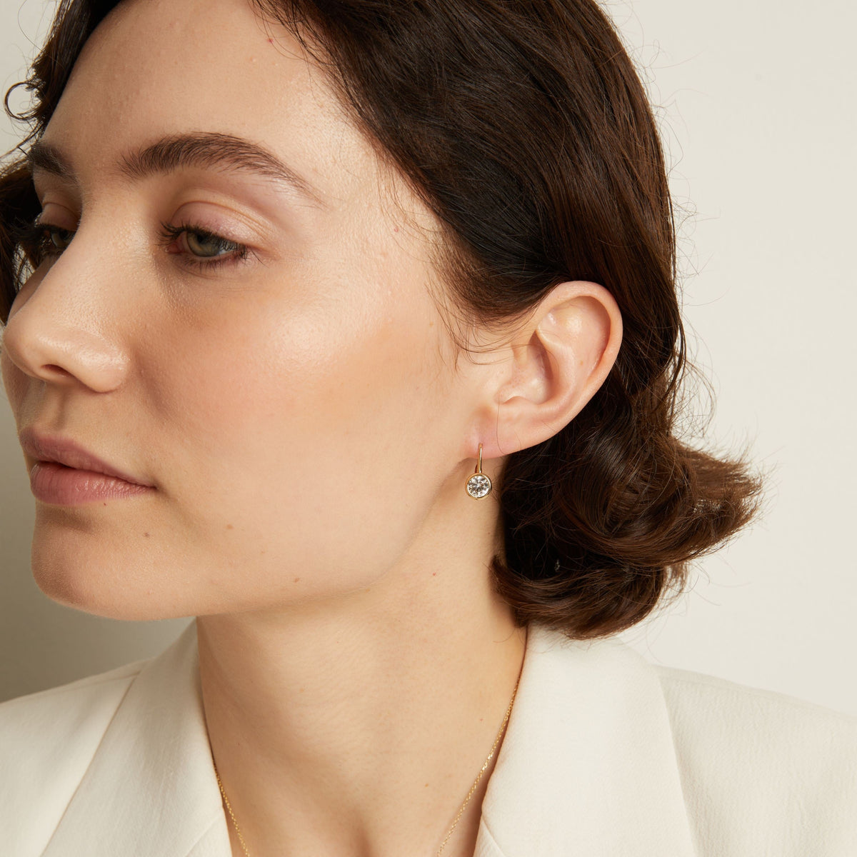 Model. Close-up of a woman wearing gemstone hoop earrings with a neutral background