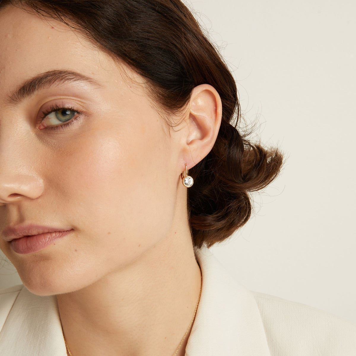 Model. Close-up of a woman wearing gemstone hoop earrings with a neutral background