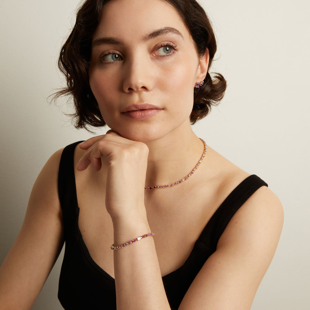 Woman wearing a pink tennis necklace and bracelet against a neutral background. Model
