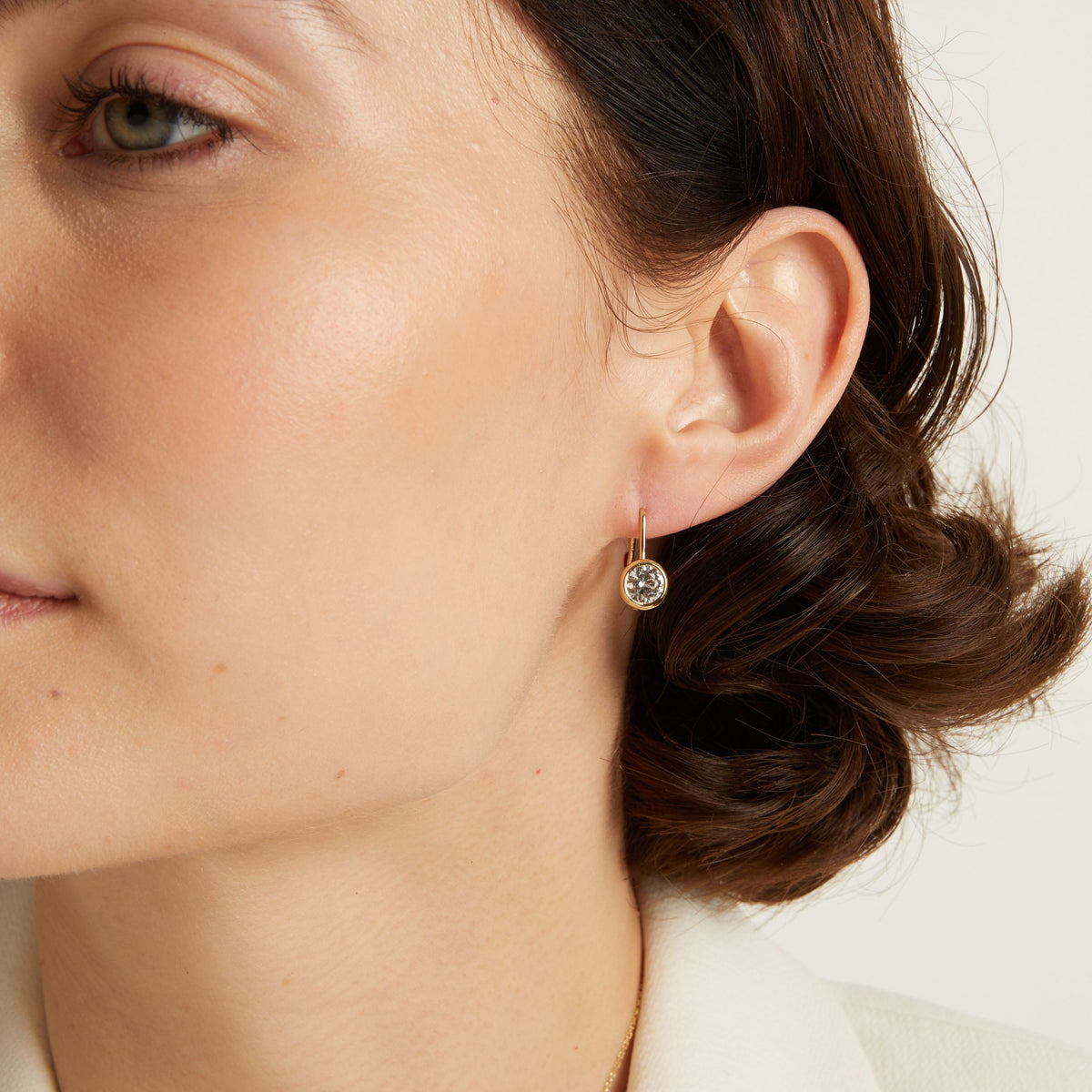 Model. Close-up of a woman wearing gemstone hoop earrings with a neutral background