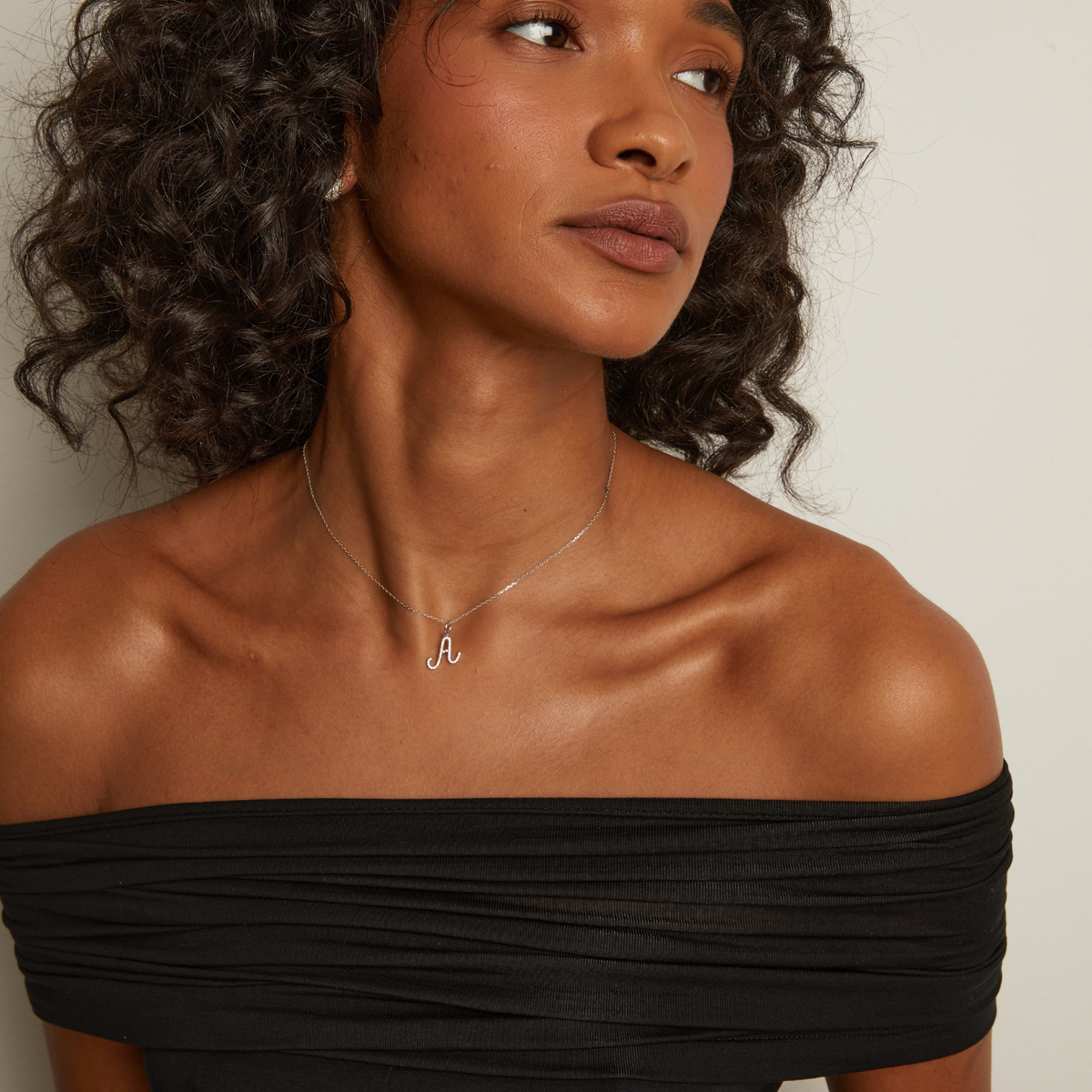 Model. Woman wearing a black off-shoulder top and a necklace with a small pendant.