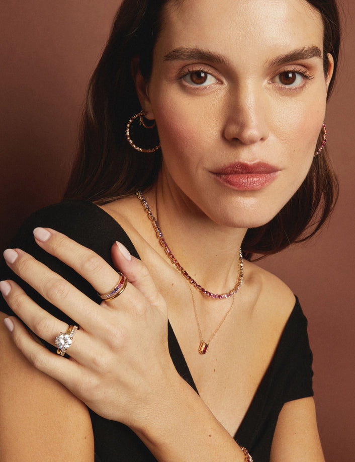 Model. Woman wearing gold jewelry including a necklace, ring, and earrings against a brown background
