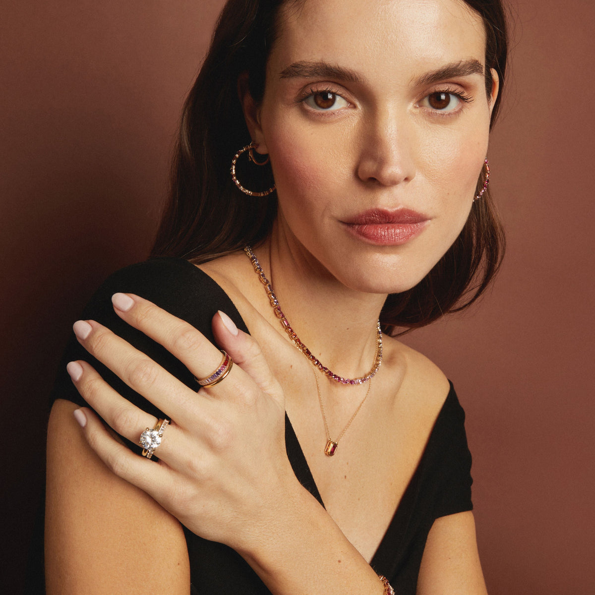 Model. Woman wearing gold jewelry including a necklace, ring, and earrings against a brown background