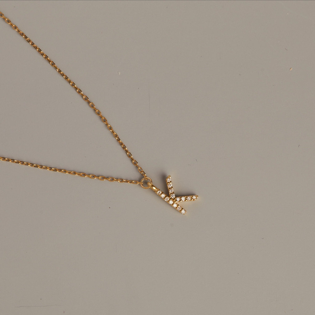 Model. Gold necklace with a 'V' pendant on a gray background