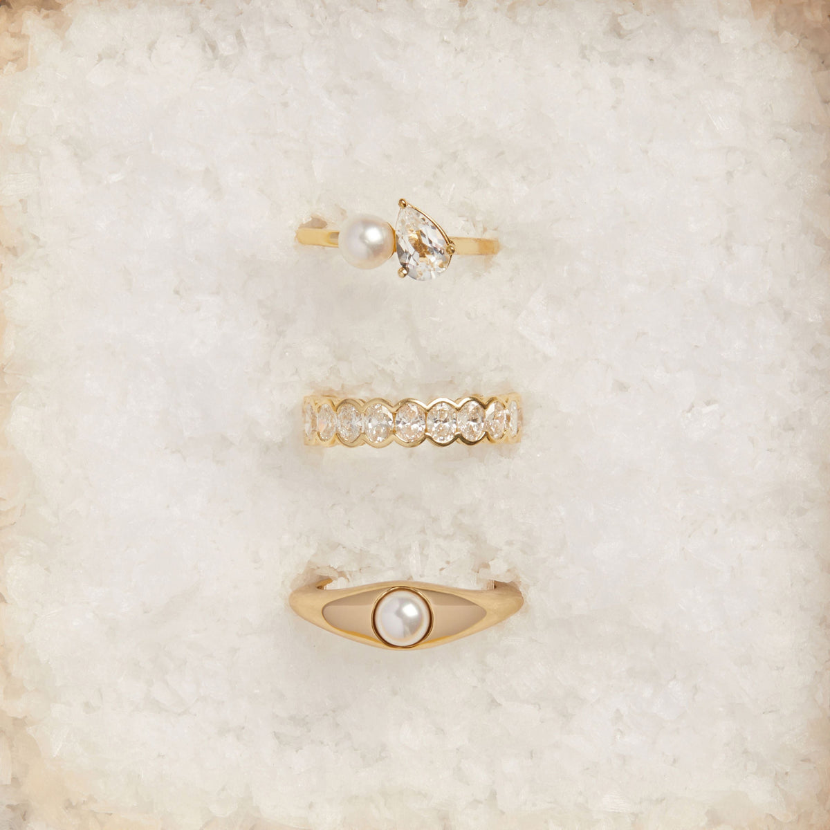 Model. Set of gold rings with pearls and crystals on a soft beige background