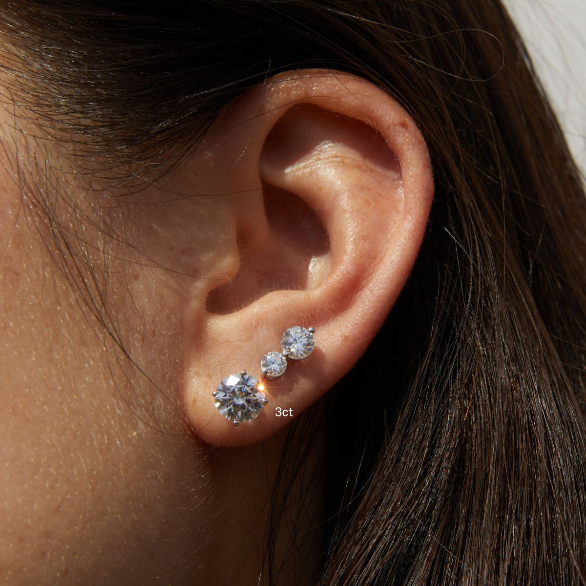 Model.  side profile of woman wearing three diamond studs 