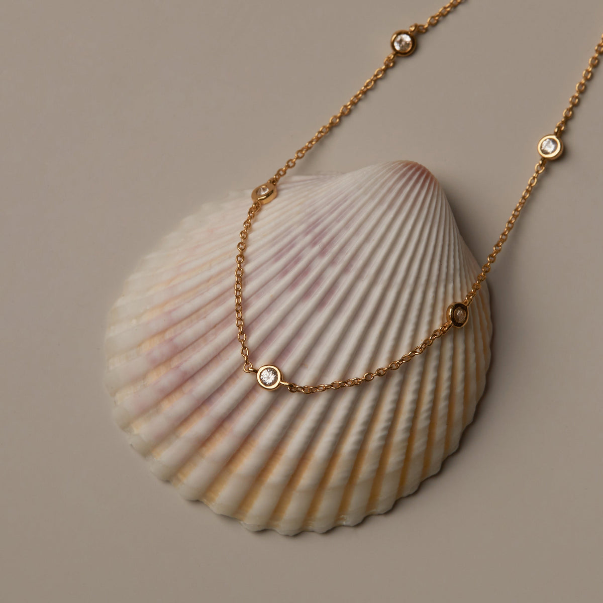 Flatlay Model. Gold necklace with small round beads on a shell against a beige background