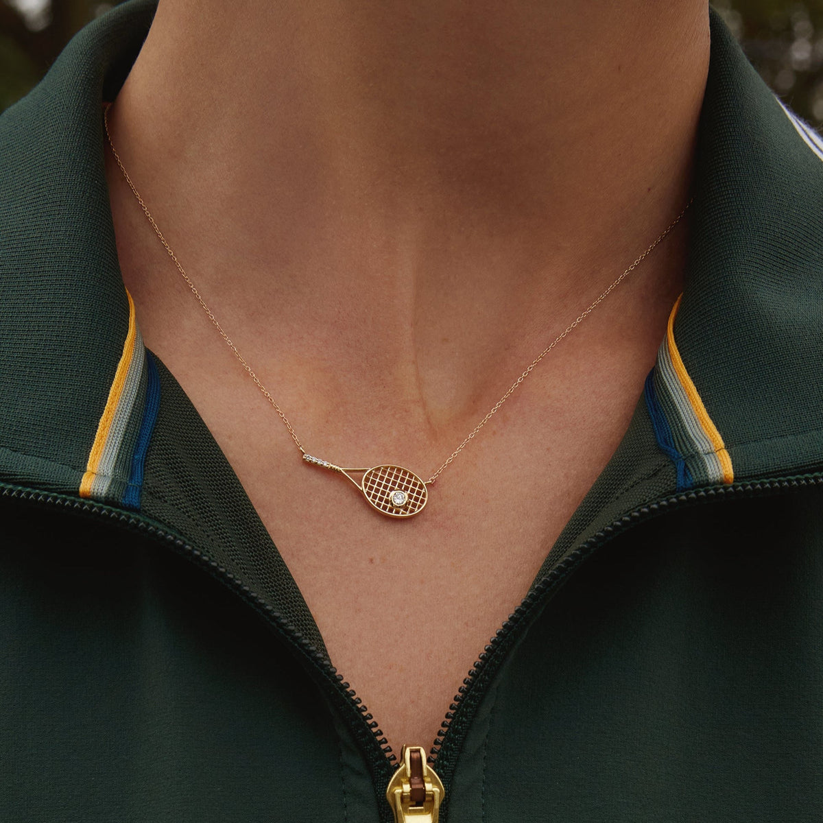 Model. Close-up of a person wearing a green jacket with a gold necklace featuring a heart-shaped pendant.