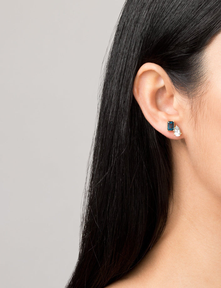 Model Close-up of a woman wearing a gold two-stone earring with a blue and a clear gemstone.