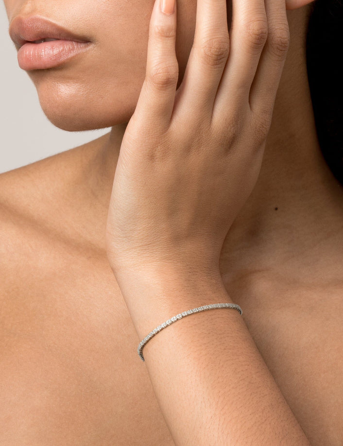 Model Close-up of a woman with her hand resting near her neck, wearing a single diamond tennis bracelet.