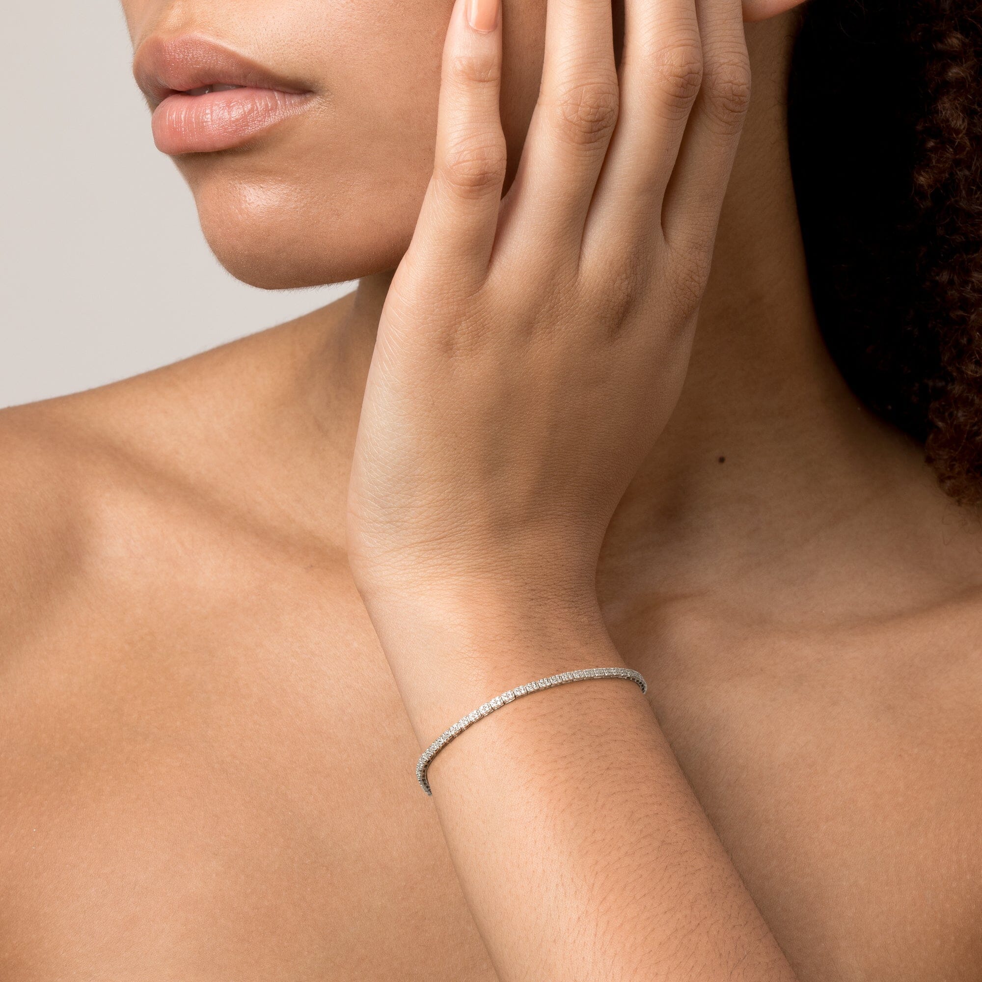 Model Close-up of a woman with her hand resting near her neck, wearing a single diamond tennis bracelet.