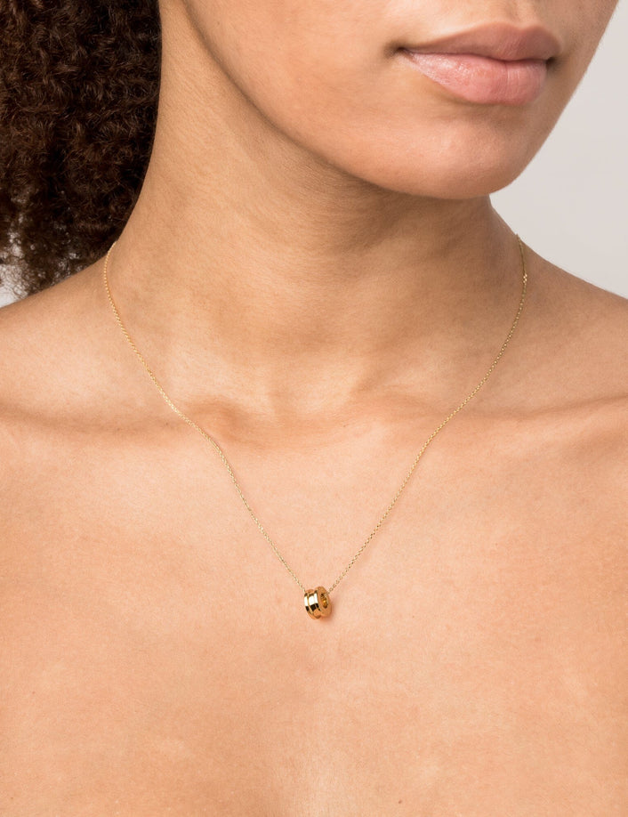 Model Close-up of a woman wearing a delicate gold chain necklace featuring a small gold column pendant