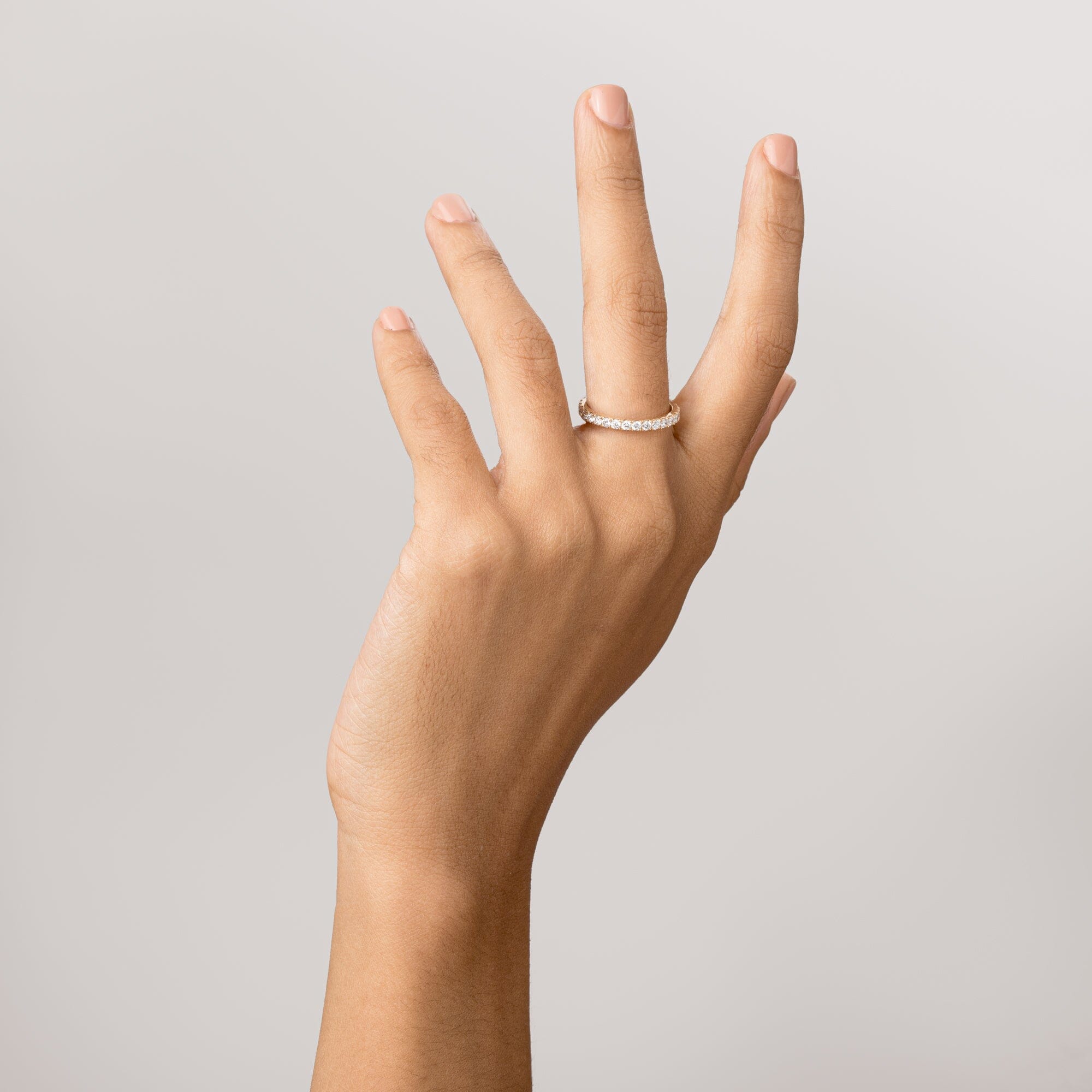 Model Close-up of a woman's hand with fingers spread upward, wearing a thin gold diamond eternity ring