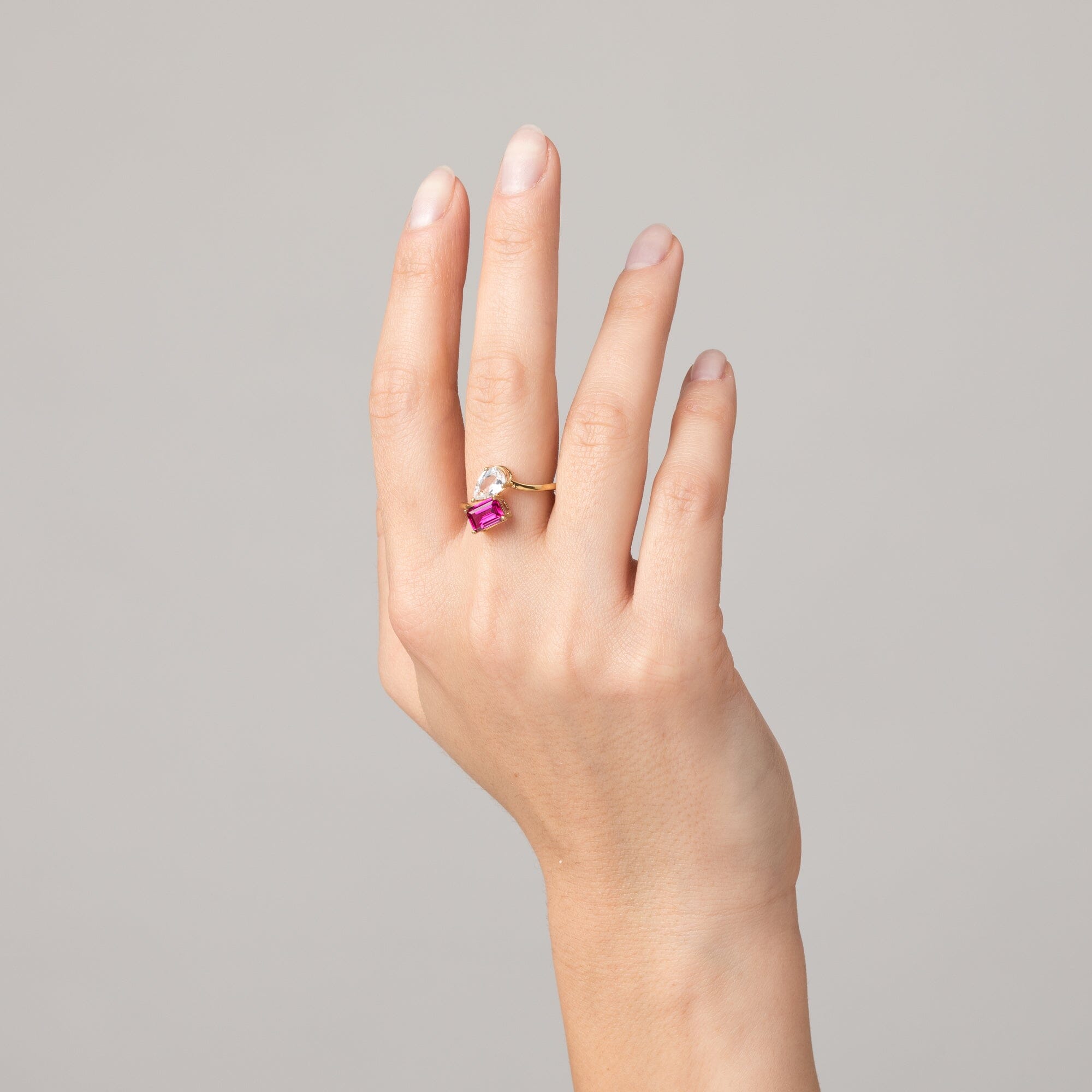 Model Close-up of a woman's hand wearing a gold two-stone ring with a clear and a pink gemstone.