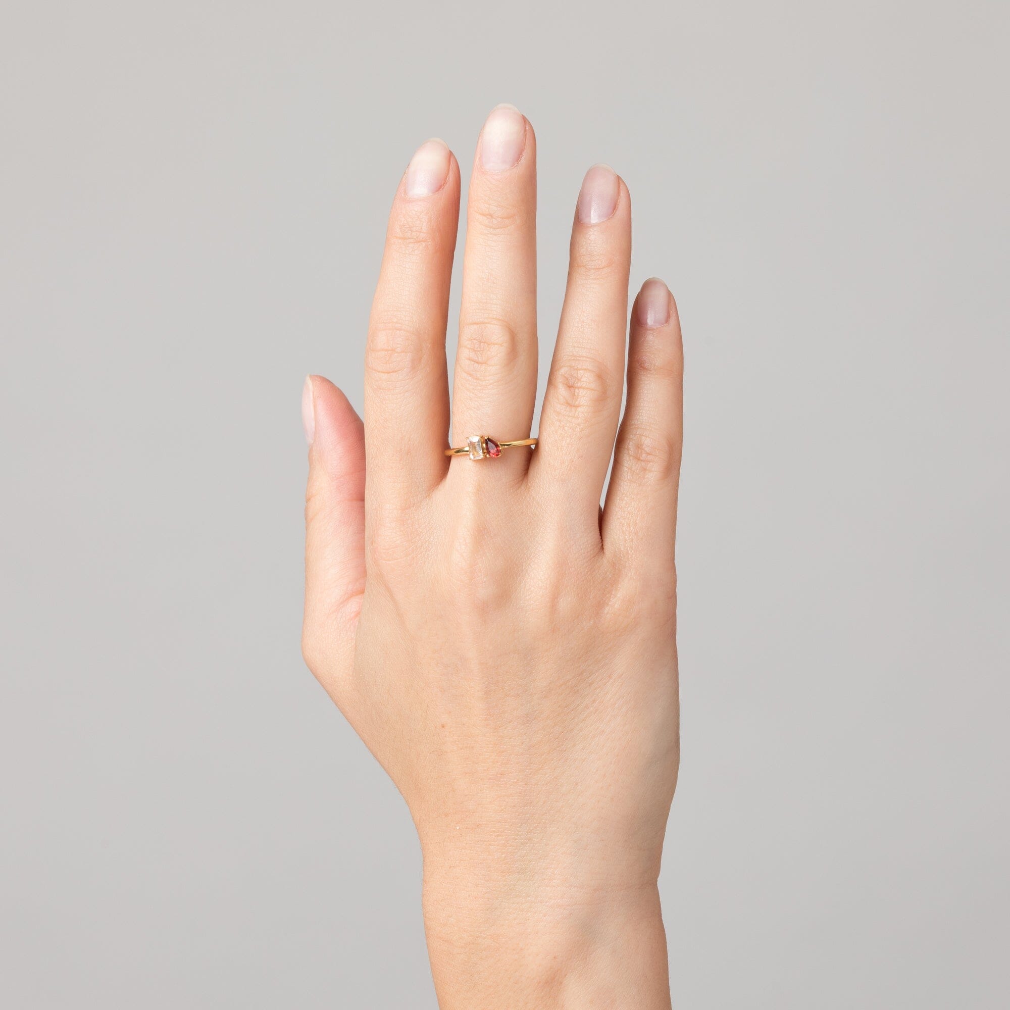 Model Close-up of a woman's hand wearing a gold two-stone ring with a clear and a pink gemstone.