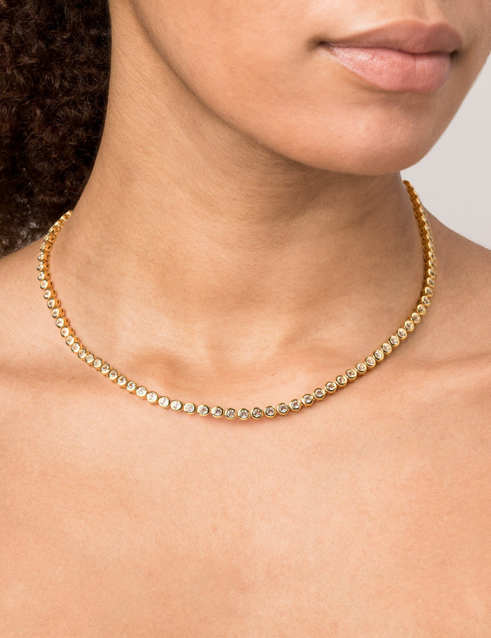 Model Close-up of a woman wearing a single gold diamond bezel tennis necklace.