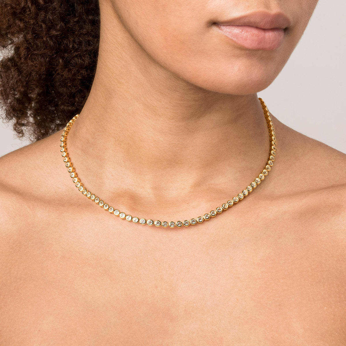 Model Close-up of a woman wearing a single gold diamond bezel tennis necklace.
