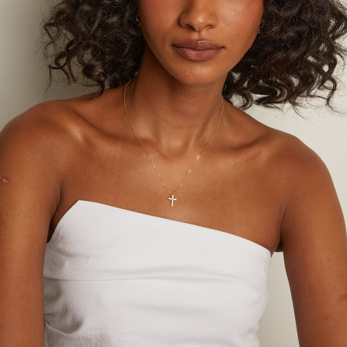 Model. Woman wearing a gold necklace with a cross pendant on a plain background