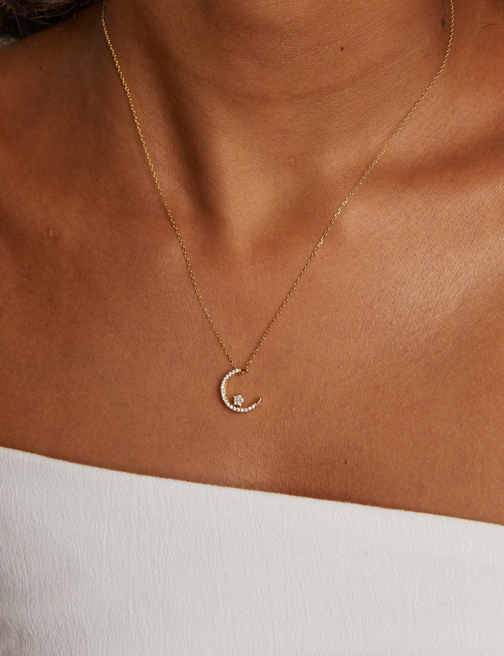 Model. Gold necklace with a moon pendant on a person wearing a white top.