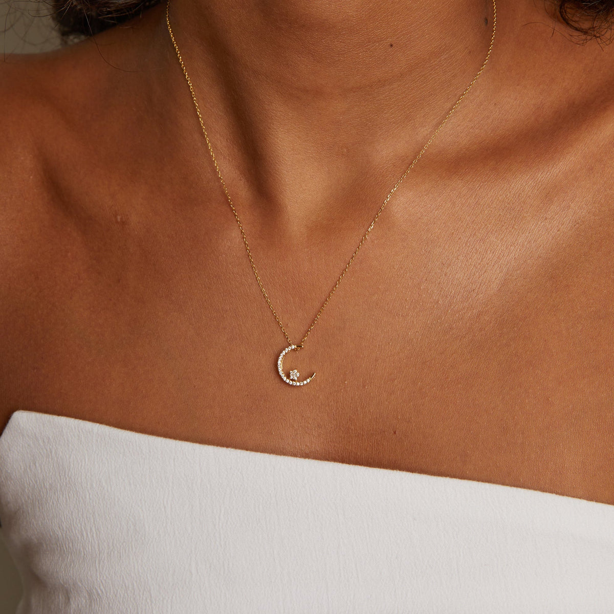 Model. Gold necklace with a moon pendant on a person wearing a white top.