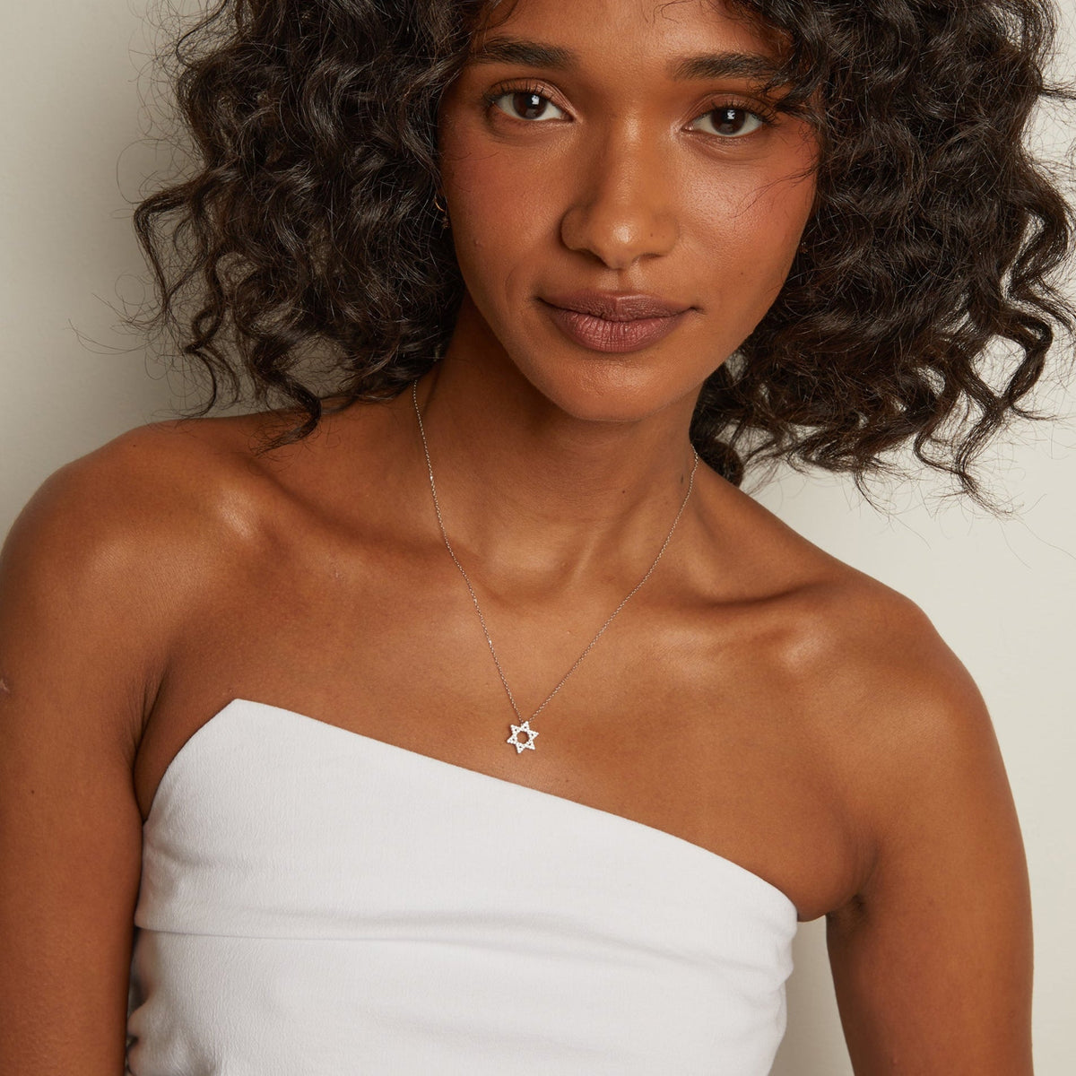 Model. Woman wearing a strapless white top and a necklace with a star pendant against a neutral background