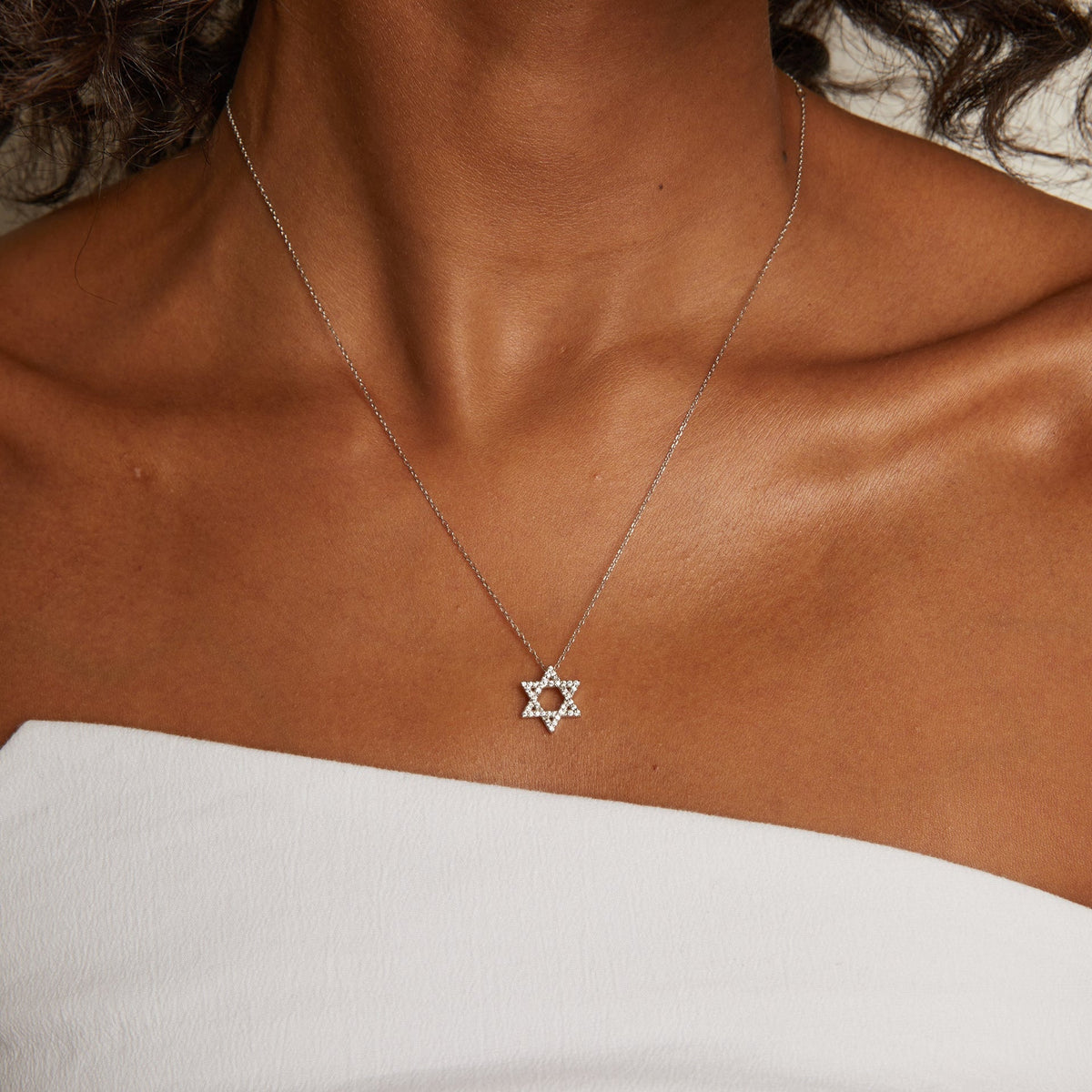 Model. Necklace with a star pendant on a person wearing a white top.