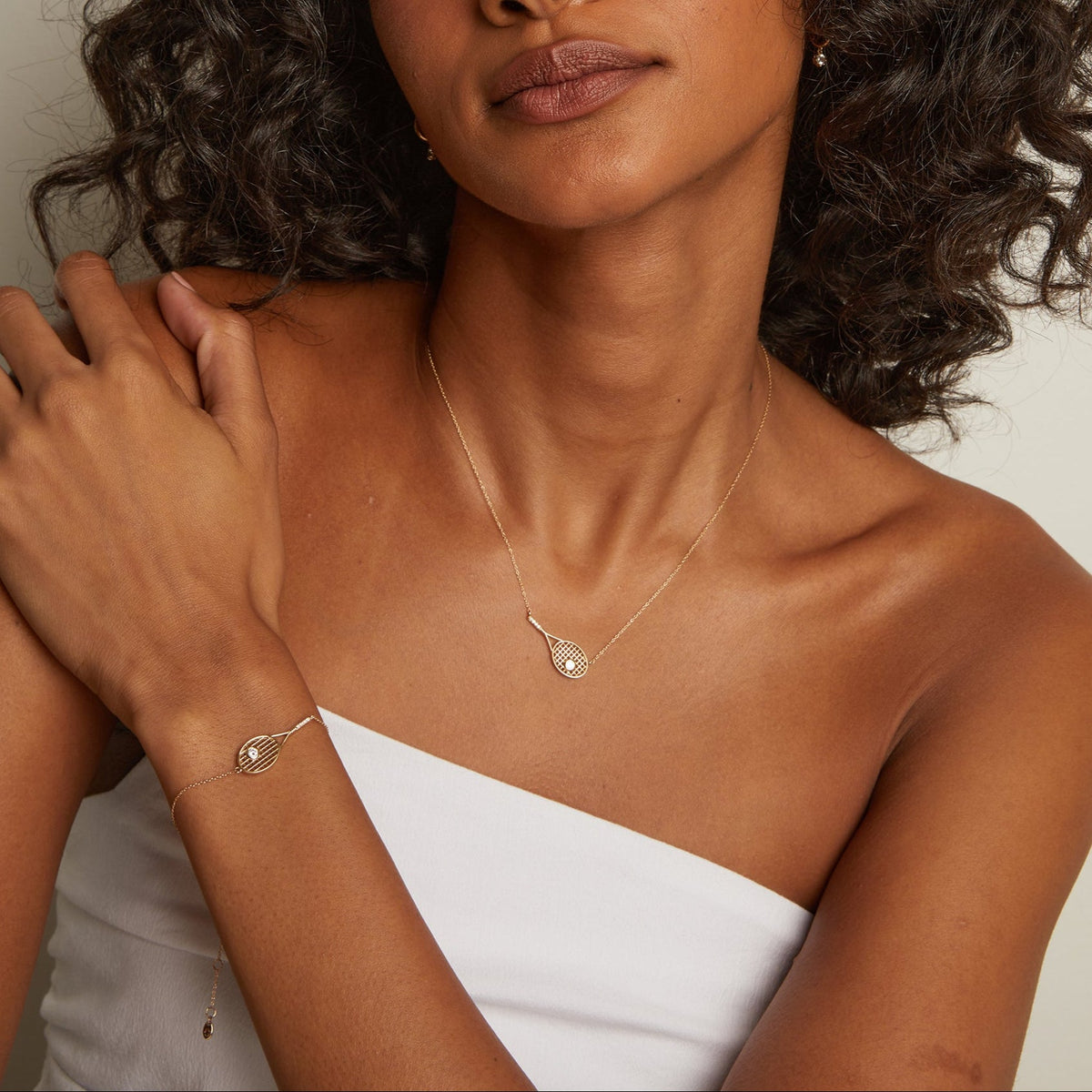 Model. Woman with curly hair wearing a white top and gold jewelry against a plain background