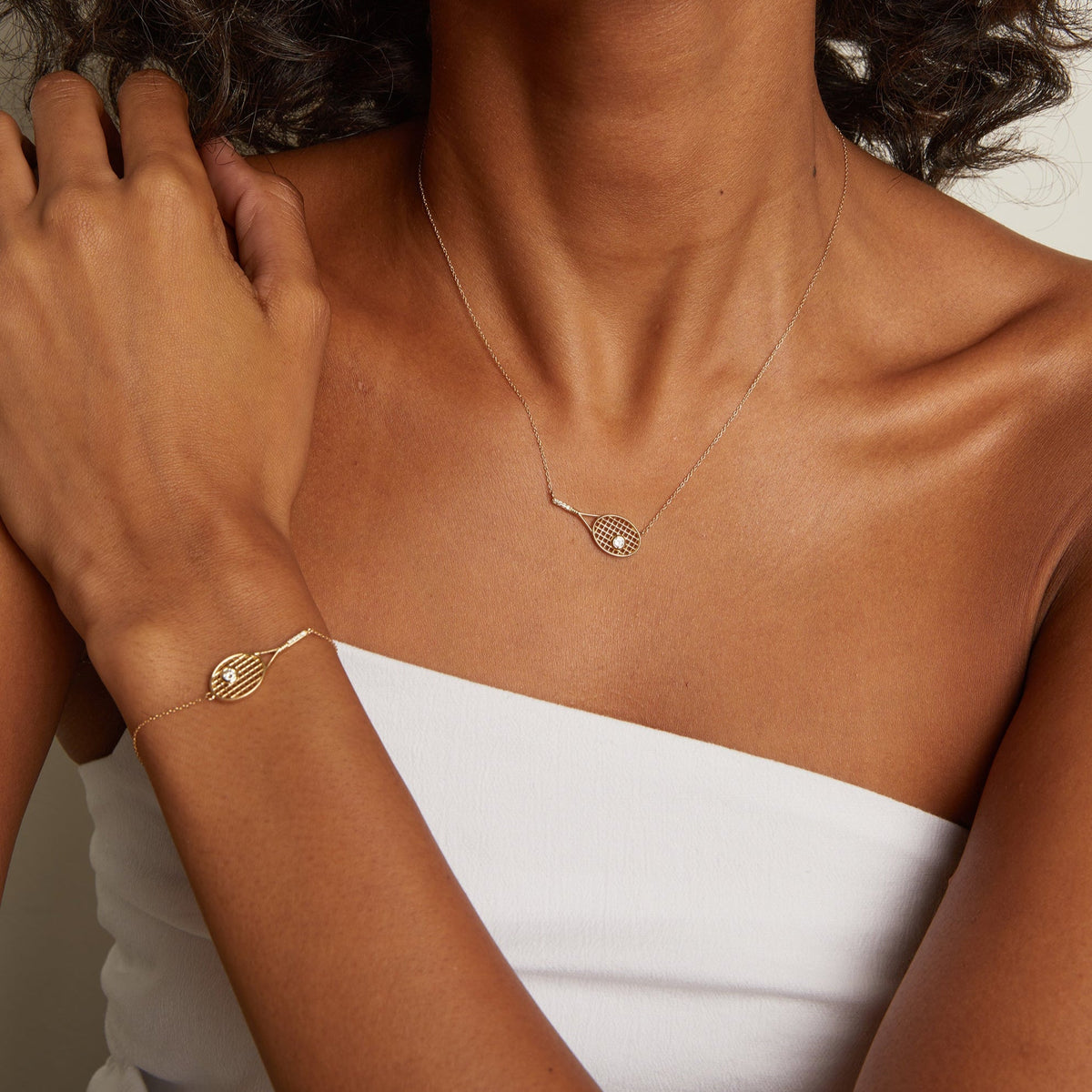 Model. Close-up of a person wearing a gold necklace and bracelet on a neutral background