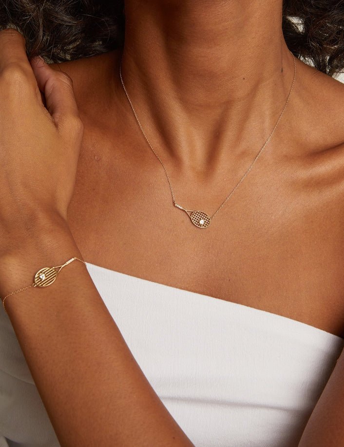 Close-up of a person wearing a gold necklace and bracelet on a neutral background