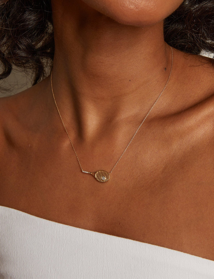 Close-up of a person wearing a gold necklace with a white top.