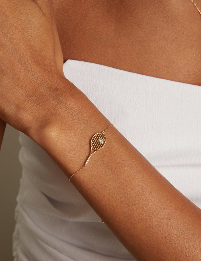Gold bracelet with a tennis racket design on a person