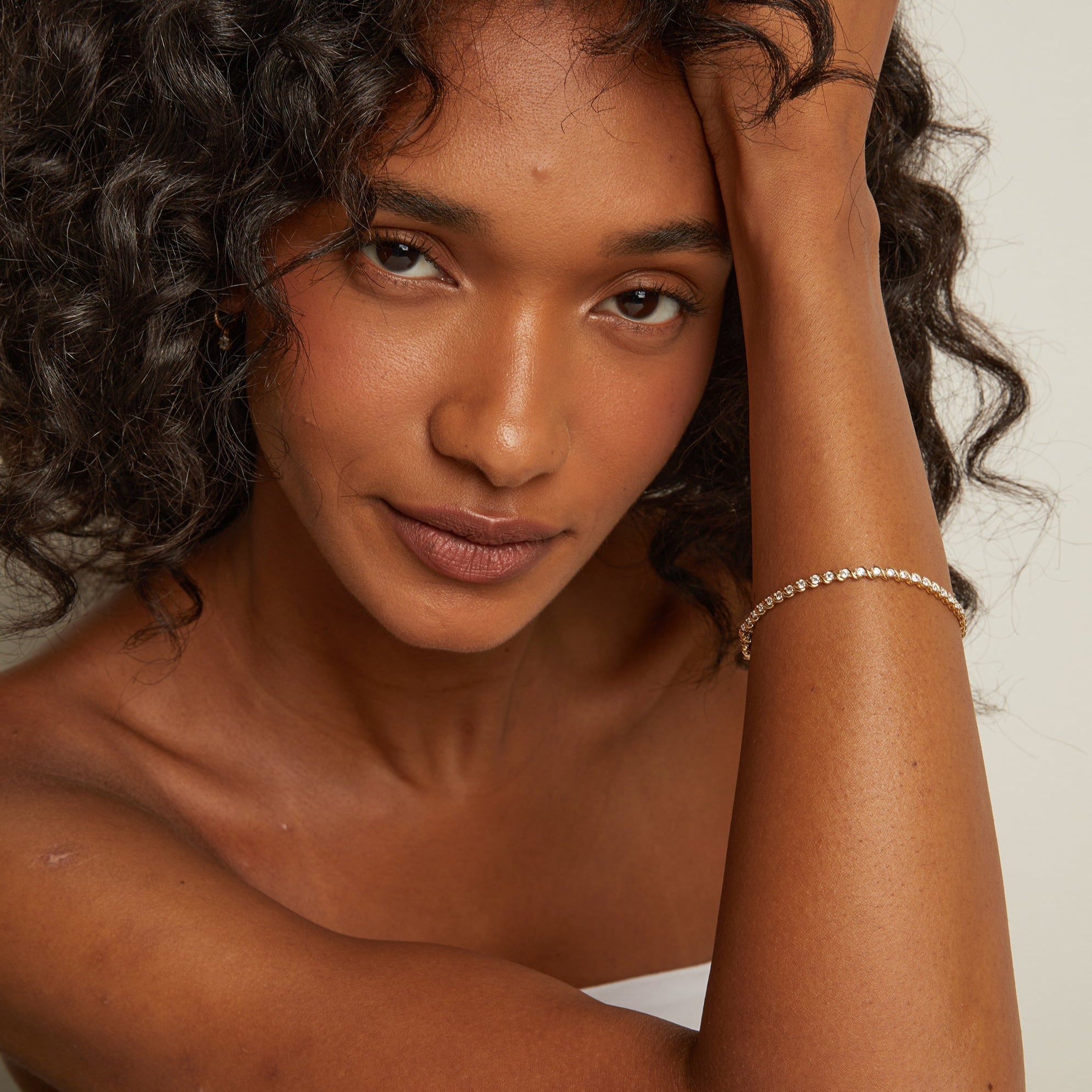 Model. Woman with curly hair touching her head against a plain background