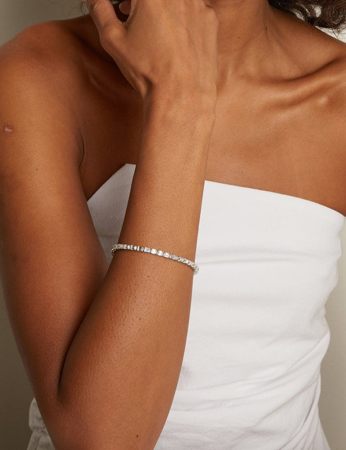 Model. Woman wearing a white strapless dress with a silver bracelet on her wrist against a neutral background