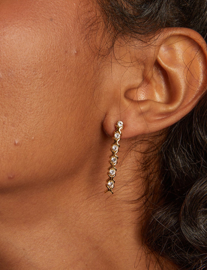 Close-up of an ear wearing a gold earring with clear stones.
