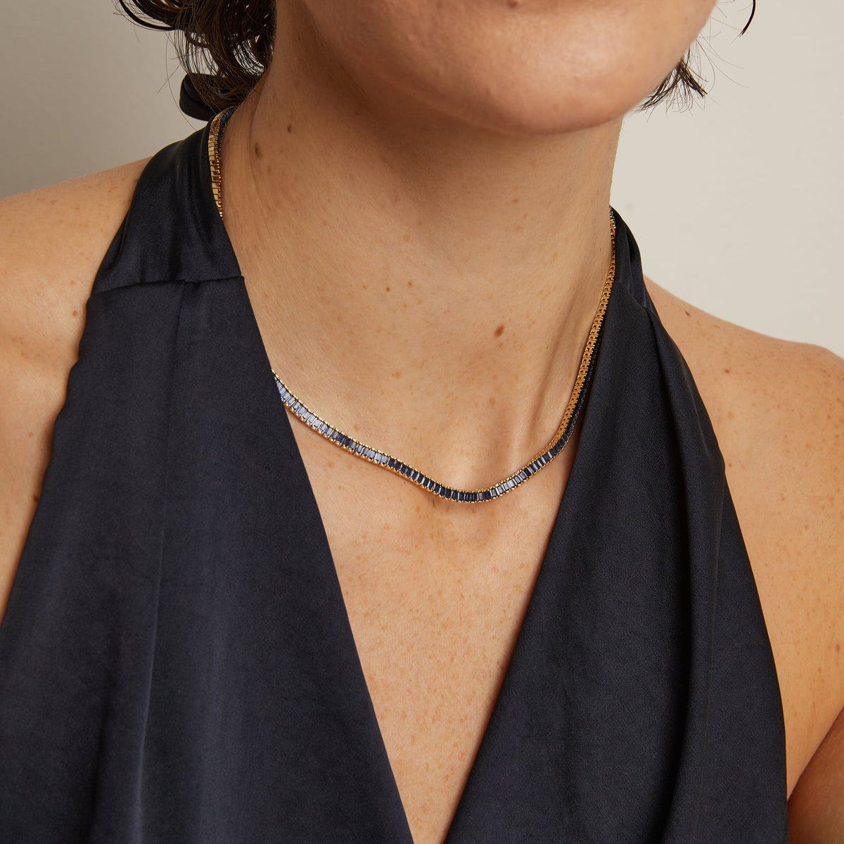 Person wearing a gold necklace with a plain background