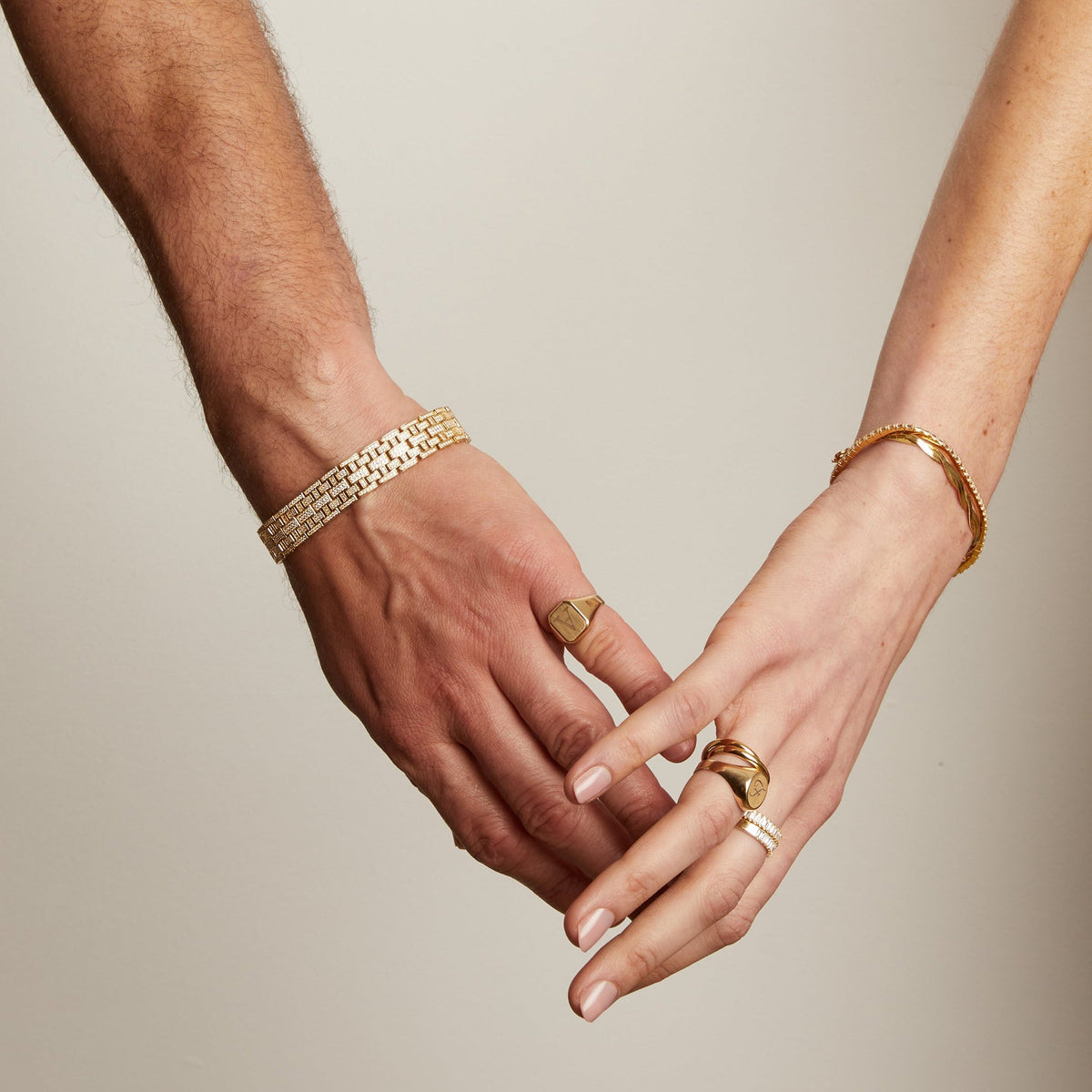 Model. Two hands holding each other with gold rings and bracelets on a neutral background
