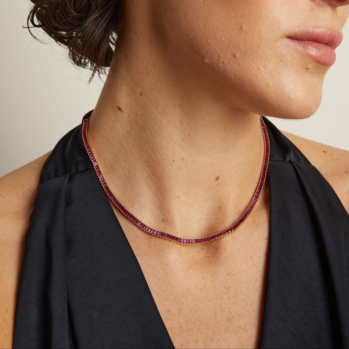 Model. Close-up of a woman wearing a red beaded necklace and earrings against a neutral background