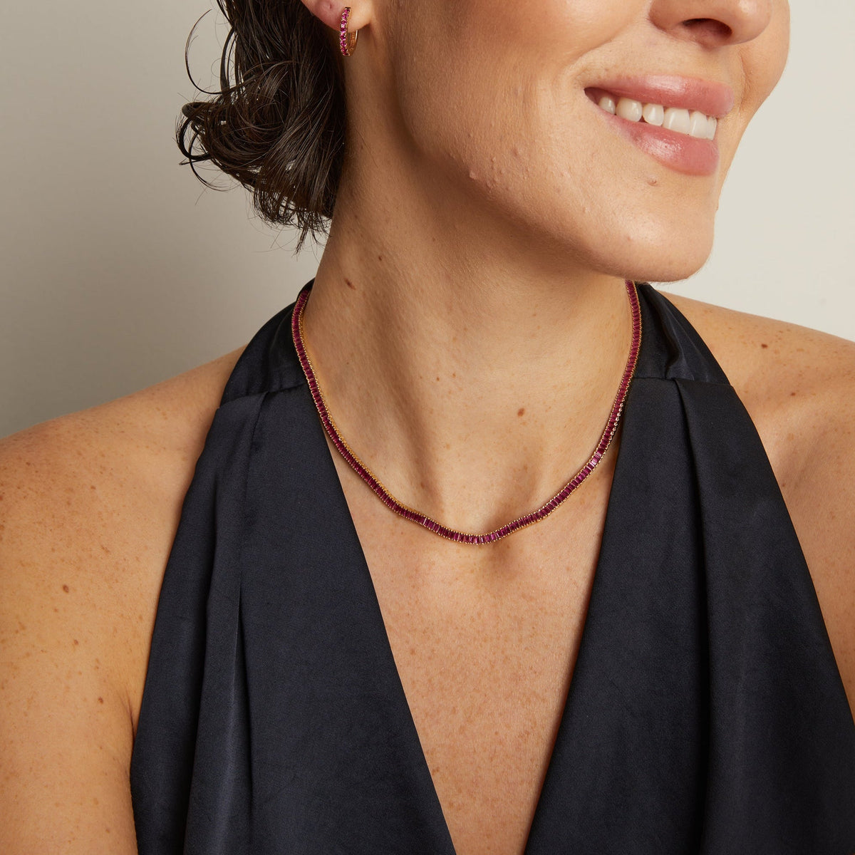 Model. Woman wearing a black halter top and red necklace against a neutral background