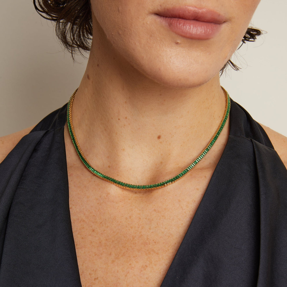 Model. Close-up of a person wearing a green beaded necklace with a plain background