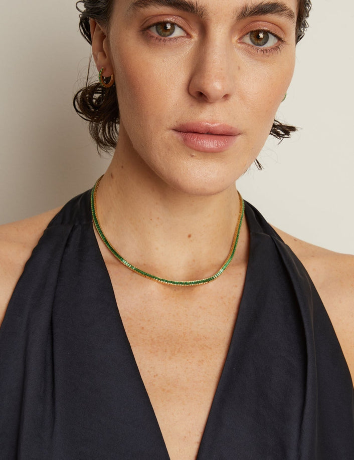 Woman wearing a black halter top and green necklace against a neutral background