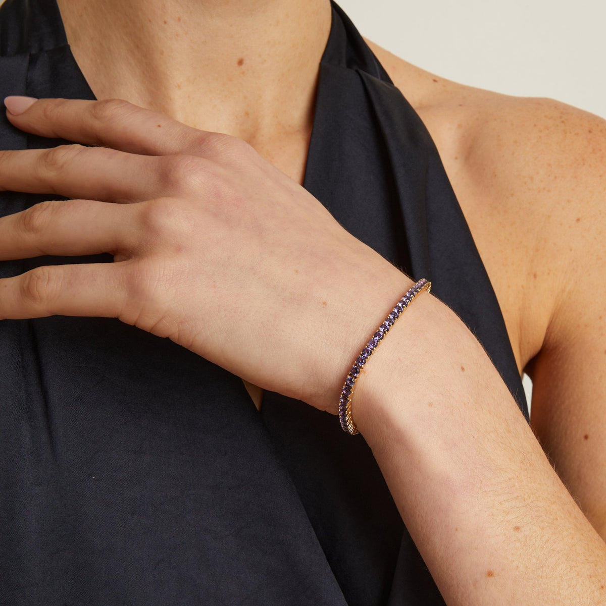 Model. Person wearing a black top with a bracelet on a neutral background