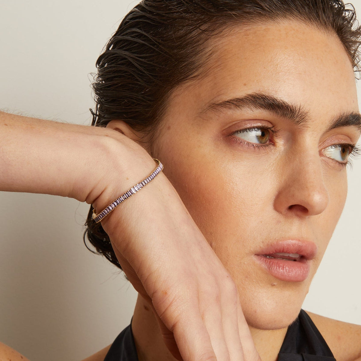 Model. Woman with a black garment and hand on her face against a neutral background