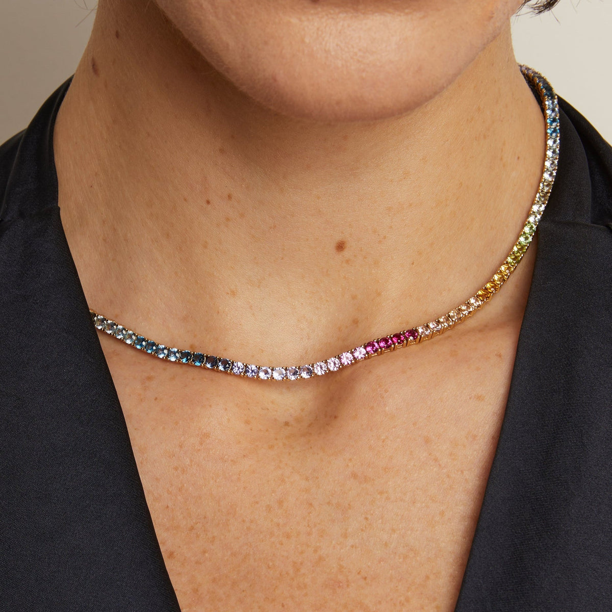 Necklace with multicolored gemstones worn by a person against a neutral background